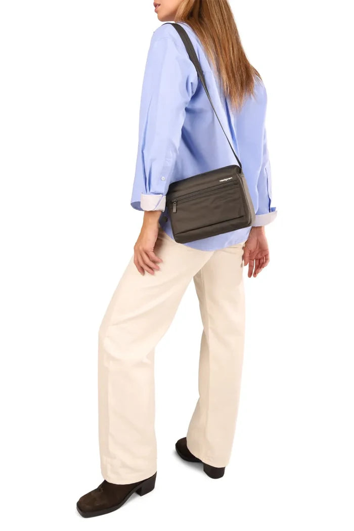 Hedgren EYE Crossbody Bag with RFID Pocket in Quilted Black, worn crossbody at the waist over a blue shirt and cream trousers