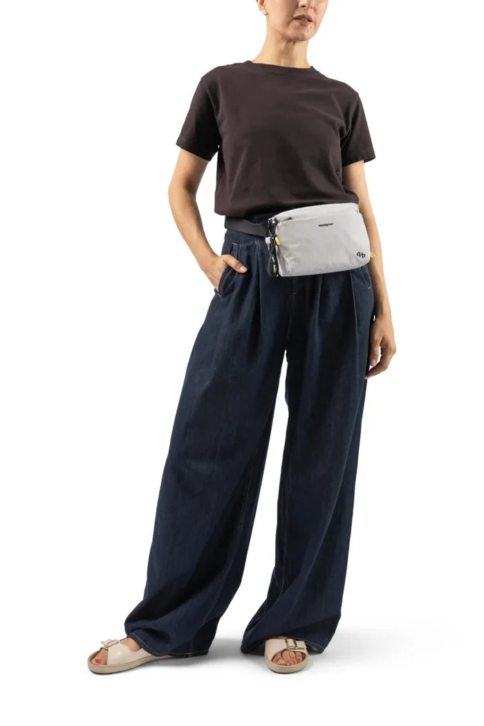 Hedgren JUN Waistbag in Black, worn at the front of the waist by a woman in a dark tee and wide denim trousers
