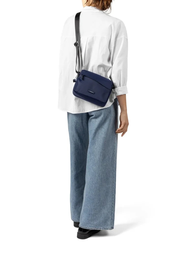 Hedgren NEUTRON Medium Crossbody Bag in Black, worn crossbody at the back by a woman in a white shirt and jeans, seen from behind