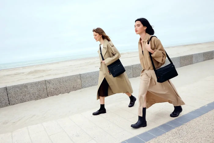 Hedgren ORVA Crossbody Bag with RFID Pocket in Black Gradient Print, worn on the shoulder by two women walking a seafront promenade in trench coats