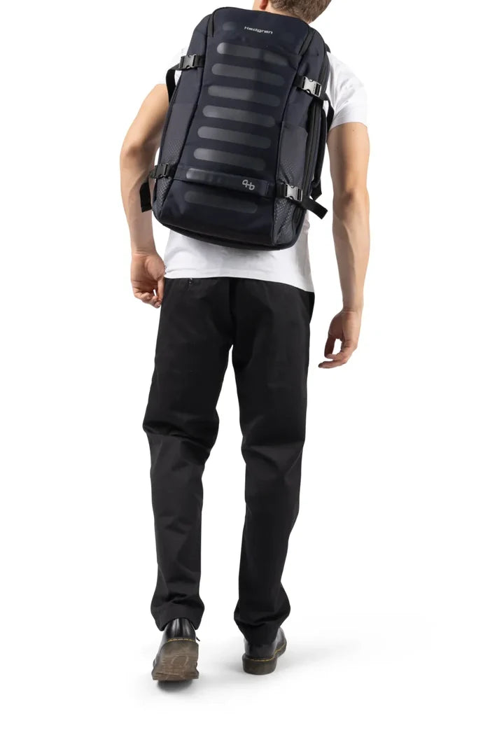 Hedgren TRIP L Expandable 15.6" Laptop Travel Backpack with RFID in Black, worn on both shoulders by a man in a white tee, seen from behind
