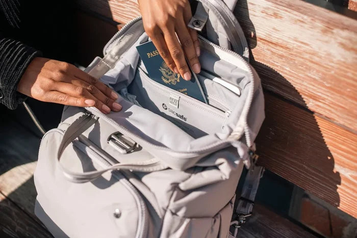 Pacsafe Citysafe CX Anti-Theft 16" Laptop Backpack in Gravity Grey, a passport being lifted from the pocket inside the open bag