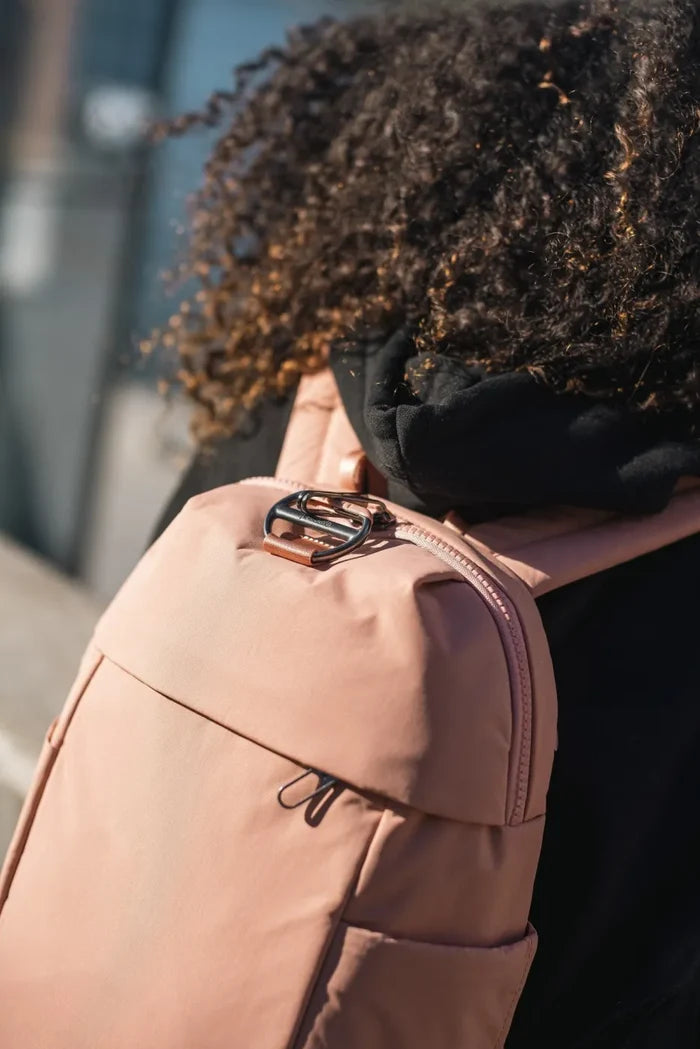 Pacsafe Citysafe CX Petite Anti-Theft 8L Backpack in Rose, worn on one shoulder with sunglasses hooked to the zip pull