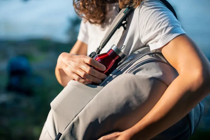 Pacsafe Eco 25L Anti-Theft 16" Laptop Backpack in Gravity Grey, a water bottle being slid into the side pocket