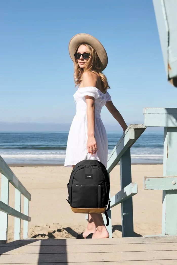 Pacsafe GO 15L Anti-Theft 13" Laptop Backpack in Jet Black, carried by the handle by a woman on beach steps
