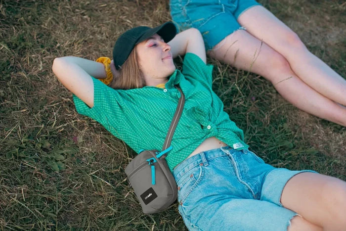 Pacsafe Go Anti-theft Micro Crossbody Bag in Stone, worn crossbody by a woman lying on the grass at a festival