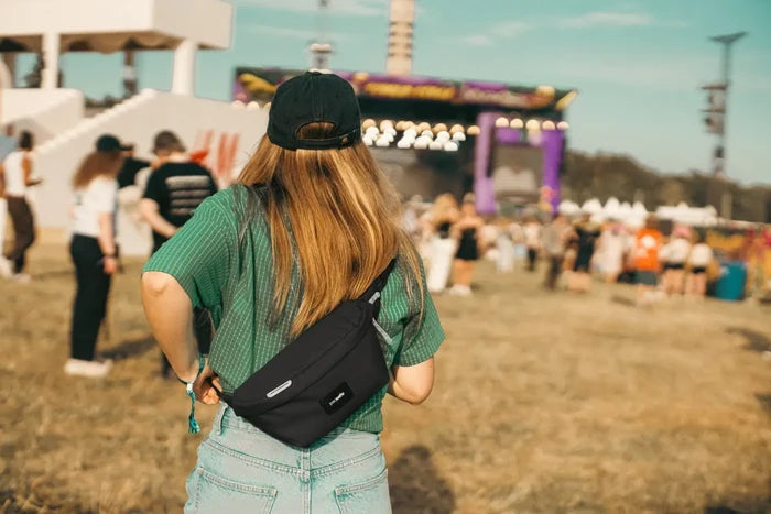 Pacsafe GO Anti-theft Sling Pack in Jet Black, worn at the back of the waist by a woman watching a festival stage