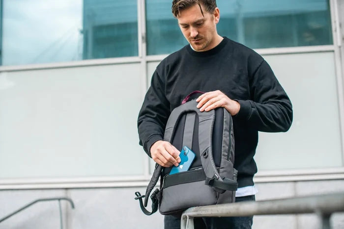 Pacsafe Metrosafe X Anti-Theft 20L 16" Laptop Backpack in Slate, a phone being taken from the pocket while the bag hangs from one shoulder