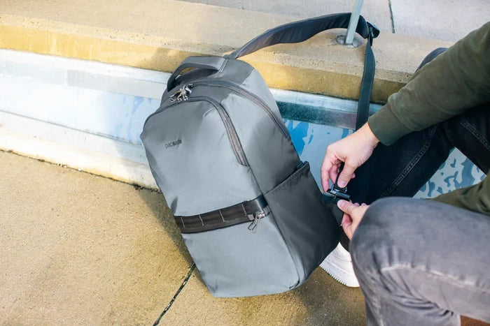 Pacsafe Metrosafe X Anti-Theft 25L 16" Laptop Backpack in Slate, the strap being locked around a kerbside rail while its owner sits