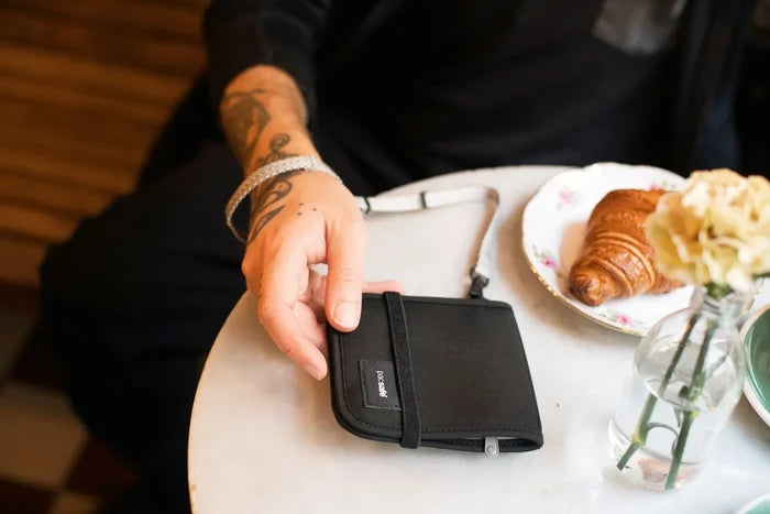 Pacsafe RFIDsafe V100 - Anti-theft RFID Blocking Bi-Fold Wallet in Black, picked up from a cafe table beside a croissant