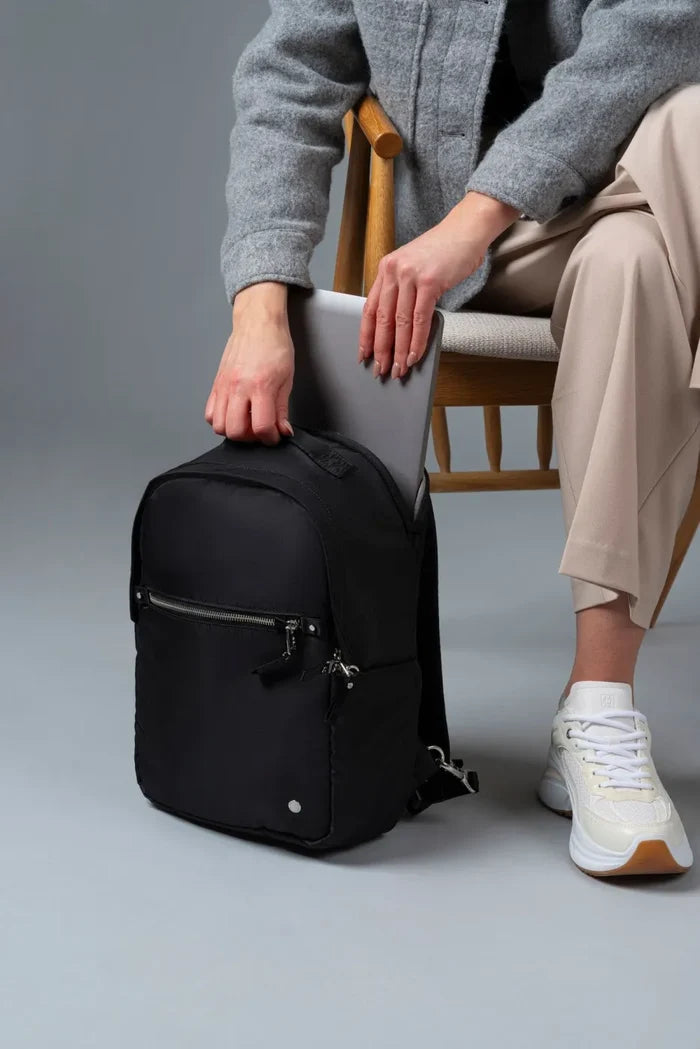 Pacsafe W 10L Anti-theft 13" Laptop Backpack in Black, a laptop being slid into the bag beside a seated woman