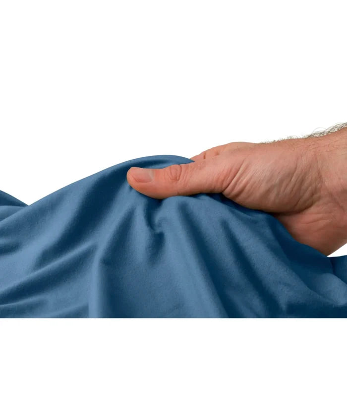 A hand gently holds a soft deep blue sea to summit drylite towel medium with subtle texture and natural folds