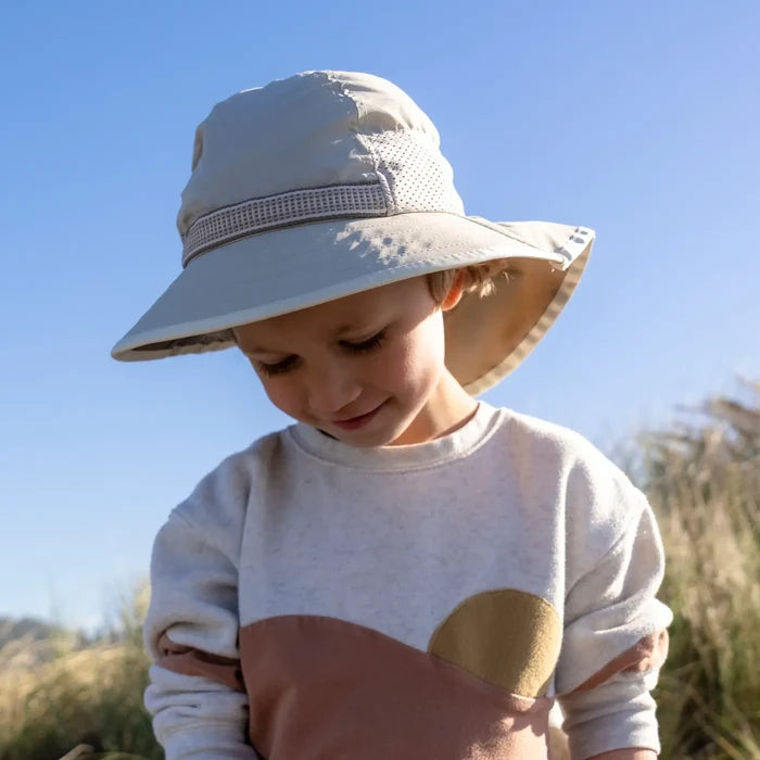 A child wearing a Sunday Afternoons Kids Play Hat on a beach